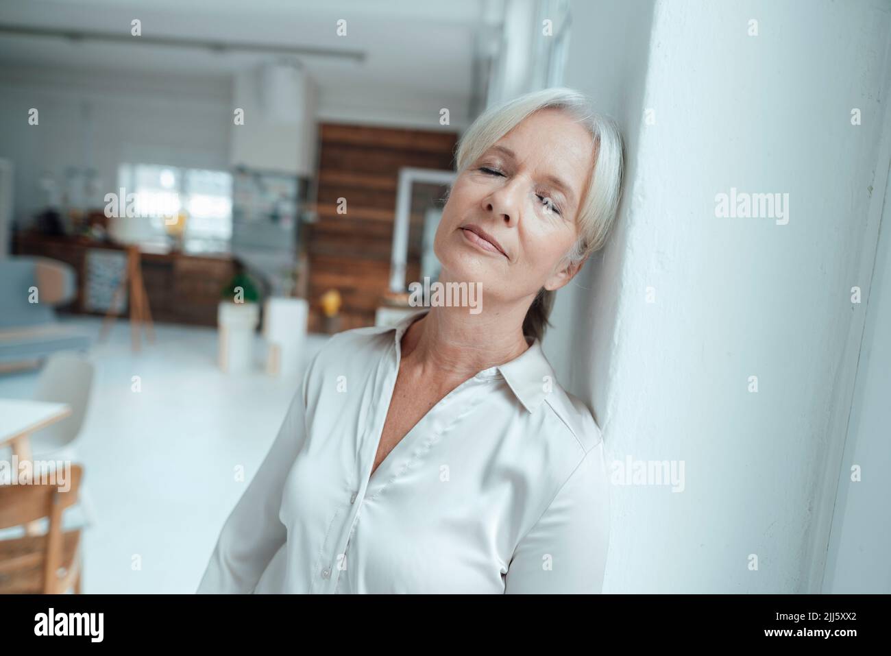 Businesswoman with eyes closed leaning on wall in office Stock Photo