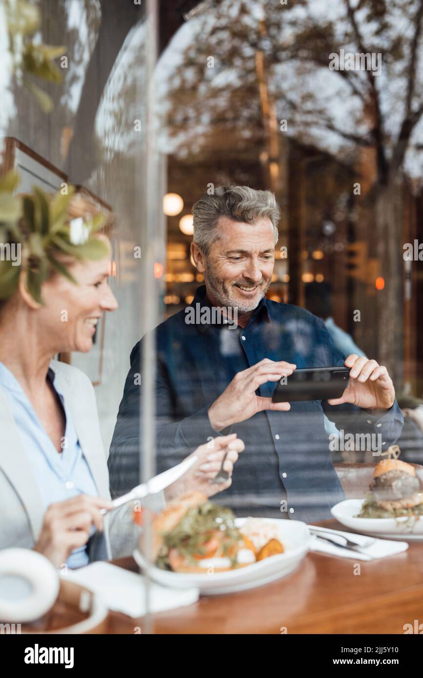 Smiling businessman photographing meal through smart phone by businesswoman in cafe Stock Photo