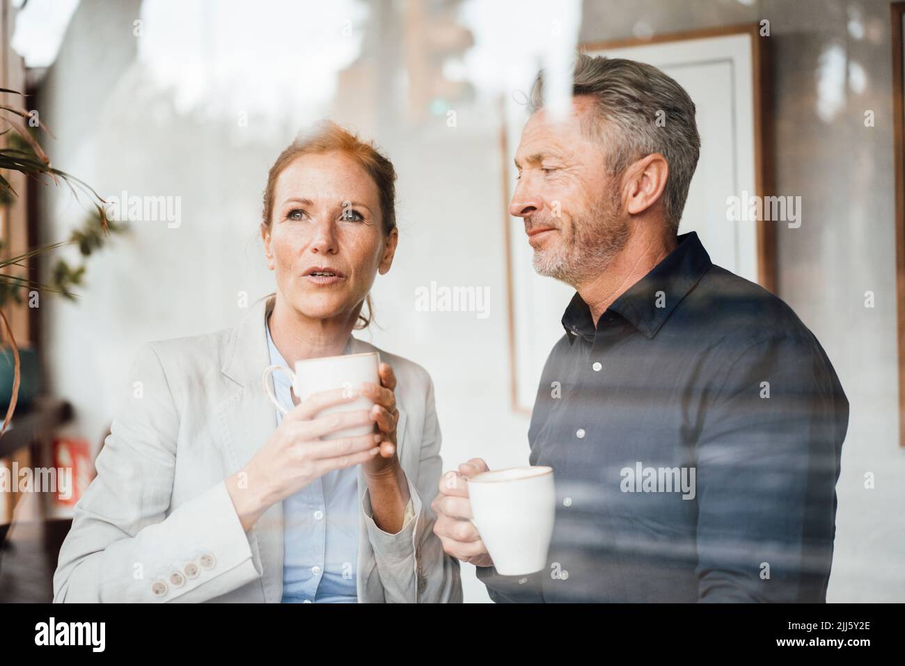 Businesswoman with businessman holding coffee cup in cafe seen through glass Stock Photo