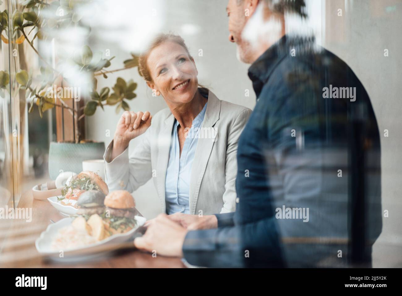 Smiling businesswoman with businessman having lunch in cafe seen through glass Stock Photo