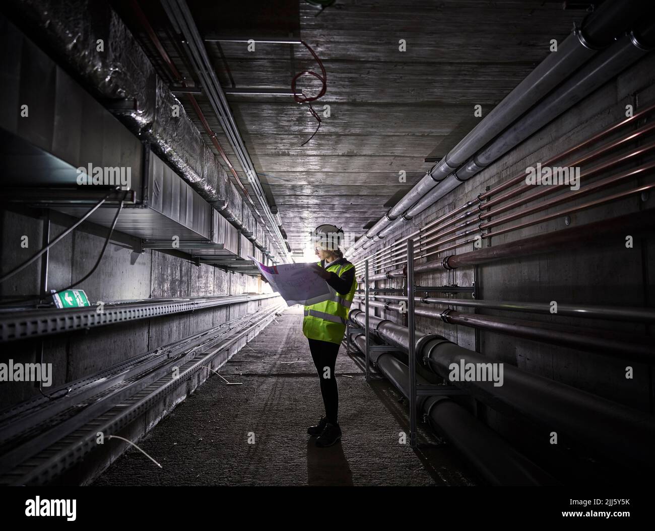 Young engineer looking at blueprint standing in tunnel Stock Photo