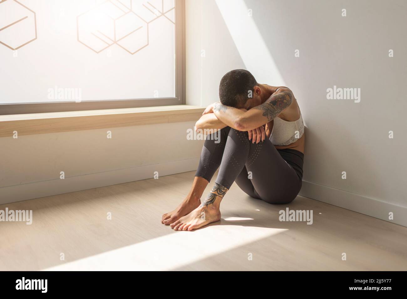 Sad woman sitting on floor by window Stock Photo