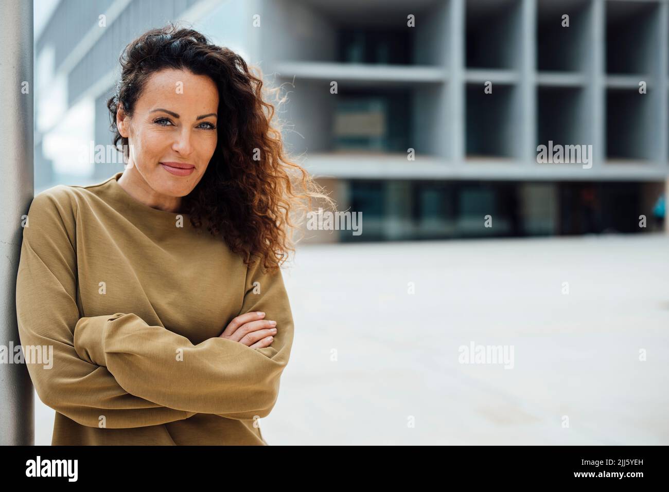 Smiling woman with arms crossed leaning on pole Stock Photo