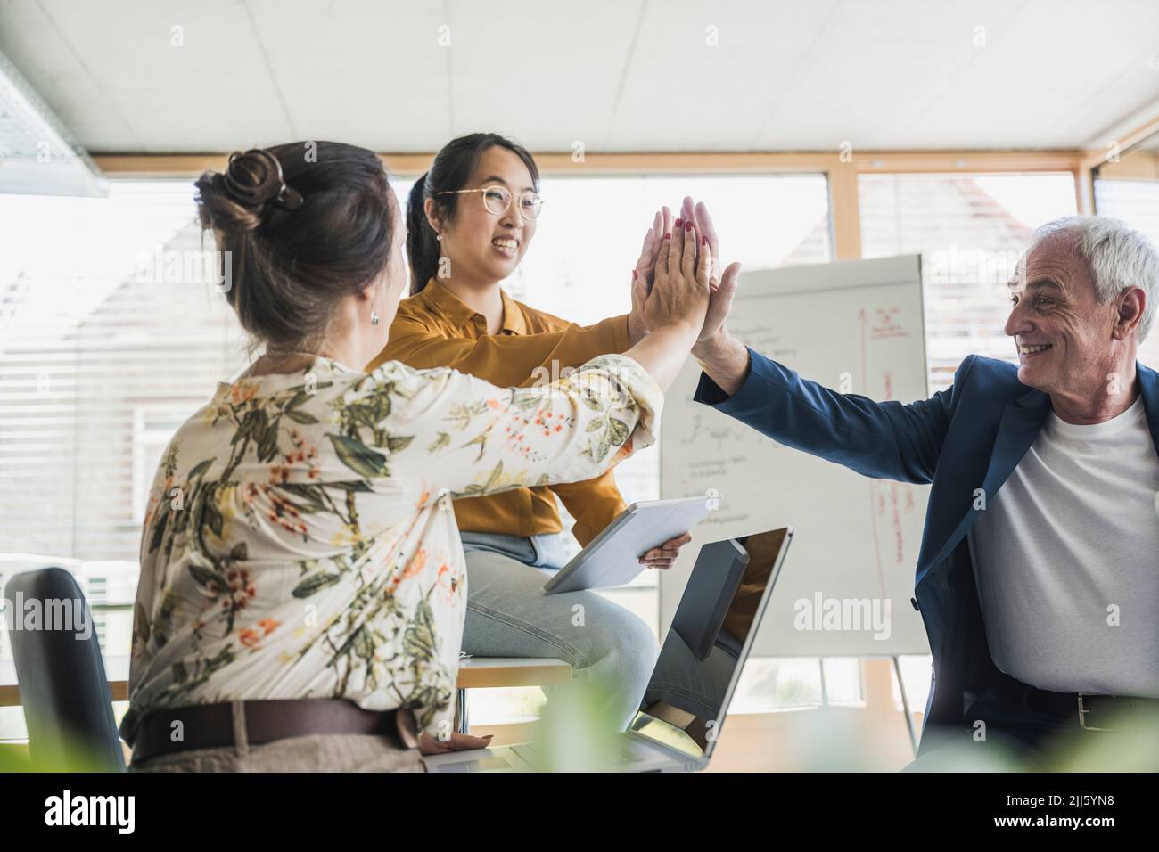 Successful business colleagues giving high-five to each other in office ...