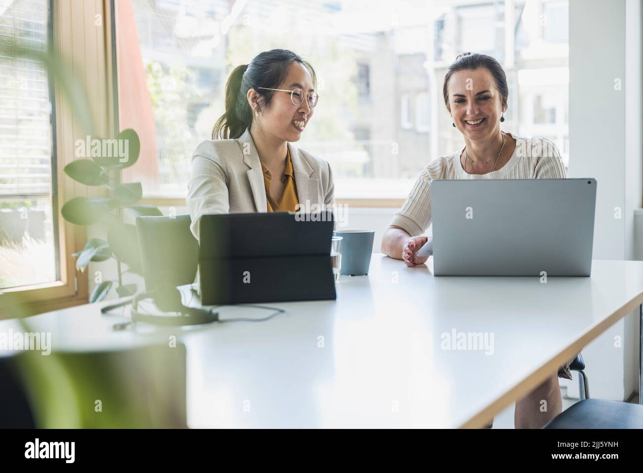 Happy mature businesswoman with colleague discussing over laptop in office Stock Photo