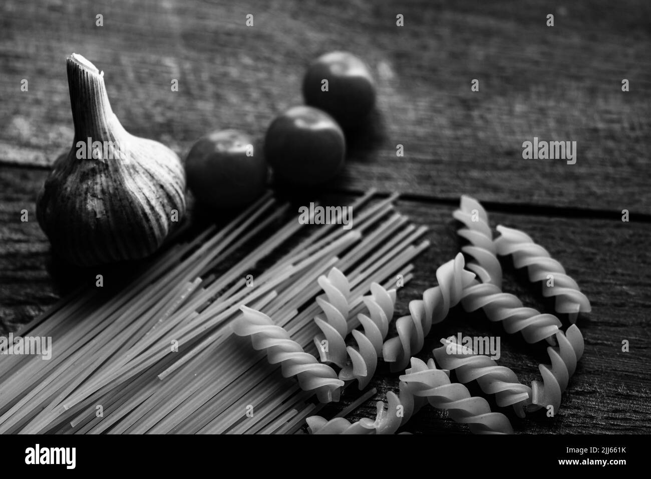 Spaghetti, cherry tomatoes and garlic on a wooden board. Stock Photo