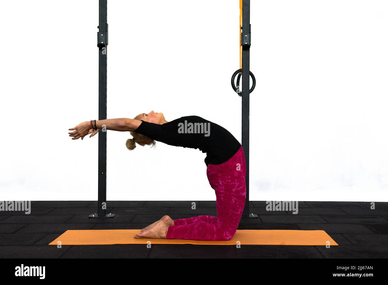 A youth lady trainer is performing the Camel yoga pose in a Gym with the two arms upwards. Ustrasana for lower back and throat stimulation. Stock Photo