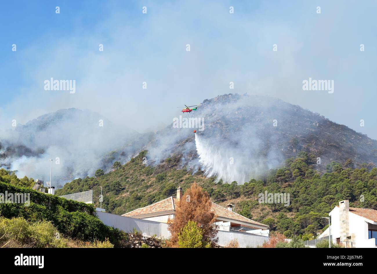 Helicopter in flight extinguishing fire approaching houses in Pinos de Alhaurin in Malaga, Spain. Stock Photo
