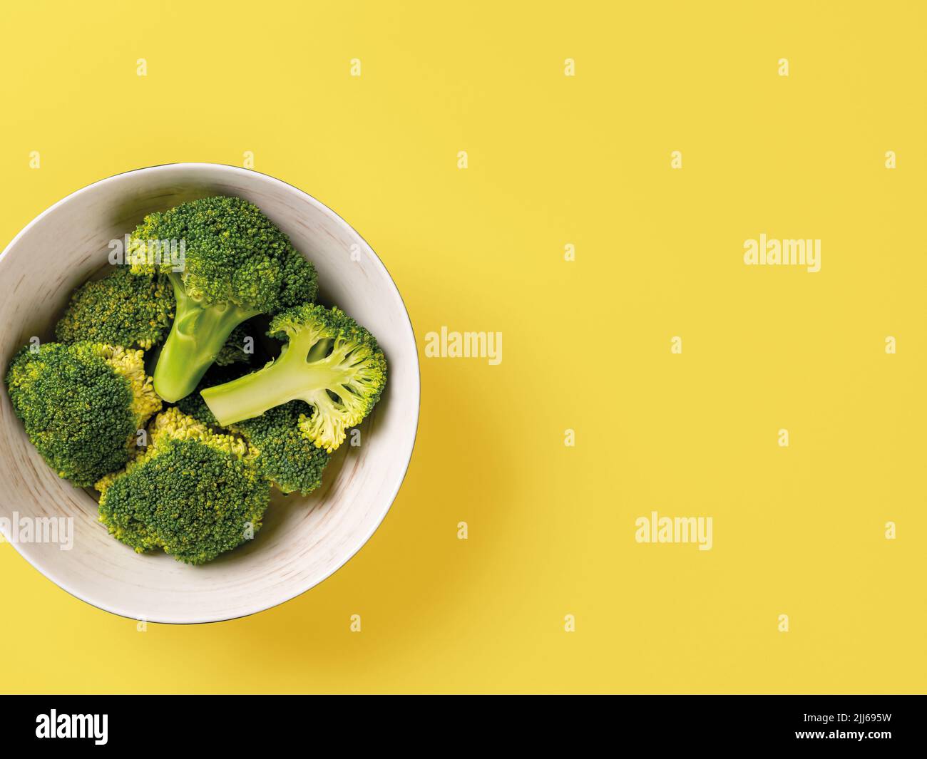 Raw green broccoli florets in a bowl against yellow background. Vitamin vegetarian food recipe. Concept low calories vegetarian dieting. Copy space. Stock Photo