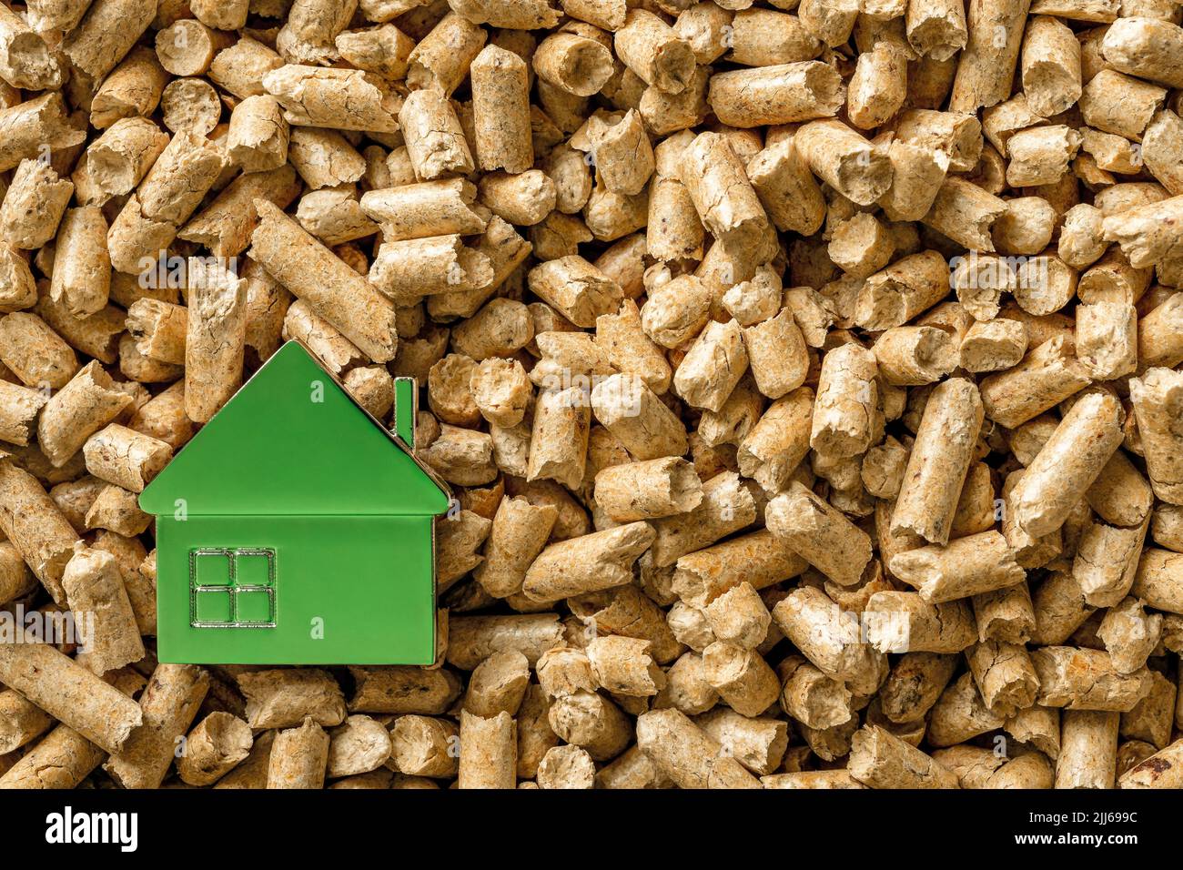 Small green house over wood pellets background. Alternative heating source for home. Organic renewable biofuel from compressed sawdust. Copy space. Stock Photo