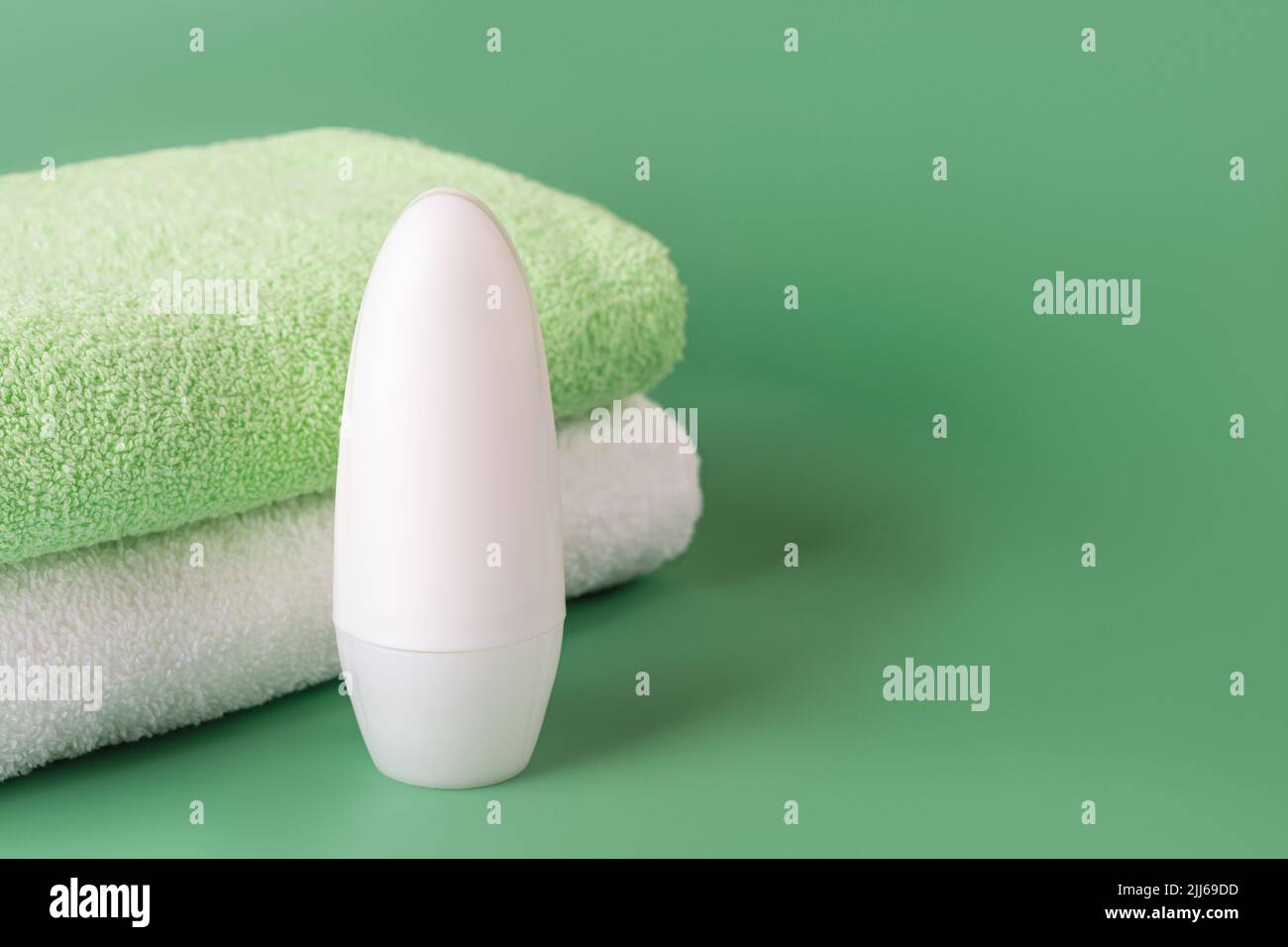 Roll on antiperspirant deodorant and bath towels on a green background. Cosmetics to reduce perspiration. Concept of personal hygiene items, body care Stock Photo