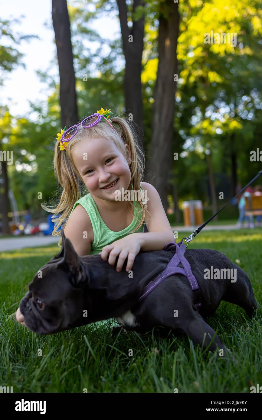 a little cheerful girl hugged a french bulldog dog and laughs merrily Stock Photo