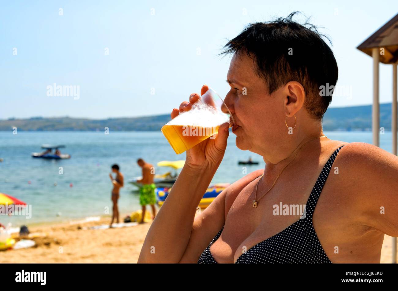 Elderly woman drinking beer on the beach. Sunny day, summer. Stock Photo