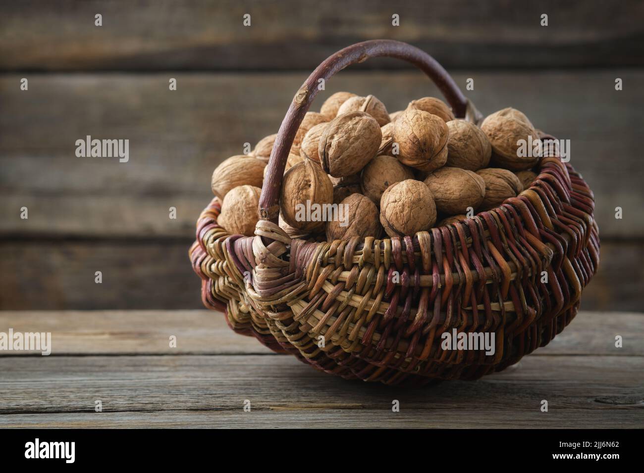 Wicker basket full of walnuts on wooden table. Stock Photo