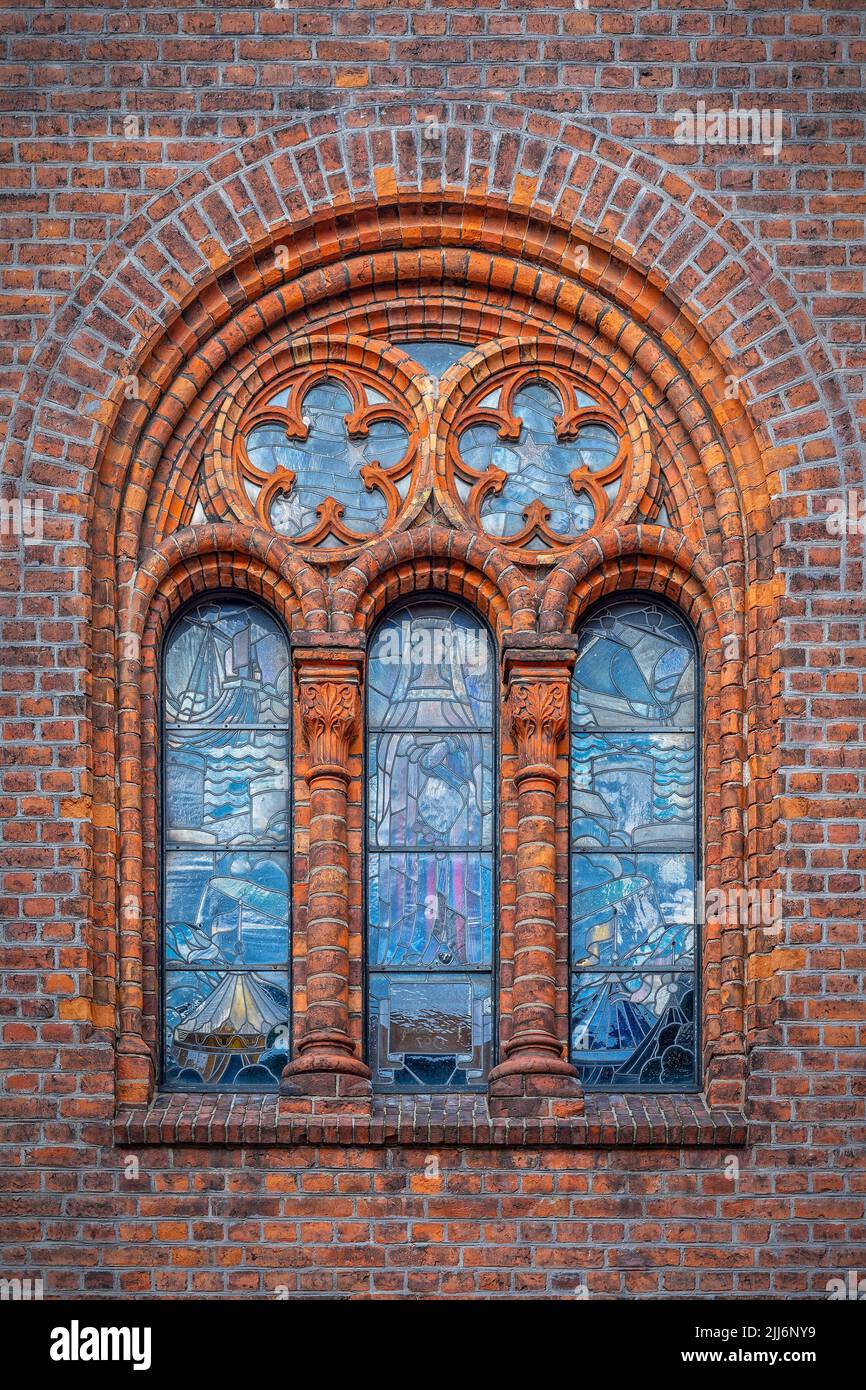 A vertical shot of an old arched window with stained glass on brick ...