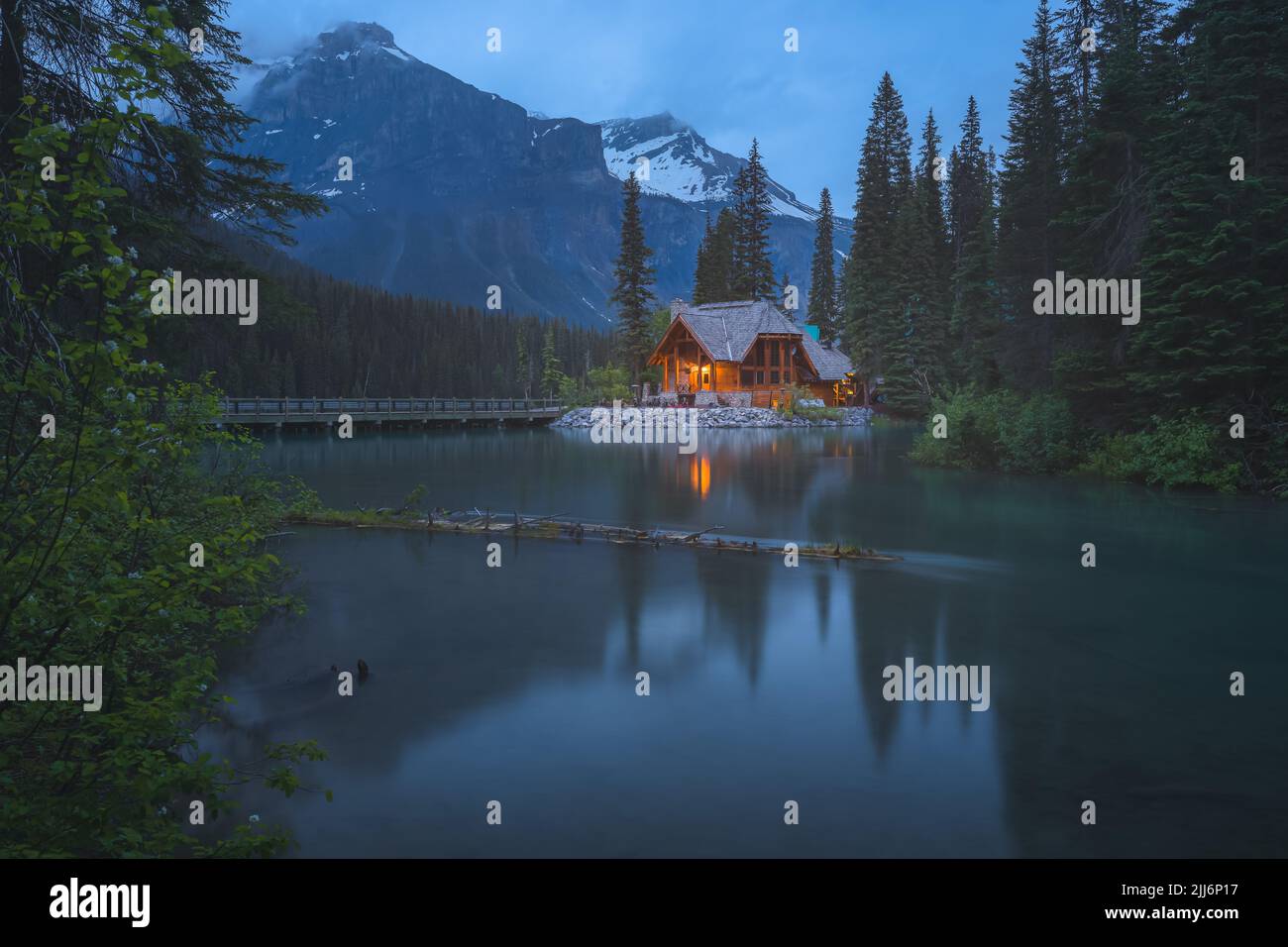 Emerald Lake, Canada - June 30, 2022: Moody, atmospheric golden light from traditional log cabin Emerald Lake Lodge at night in Rocky Mountains in Yoh Stock Photo