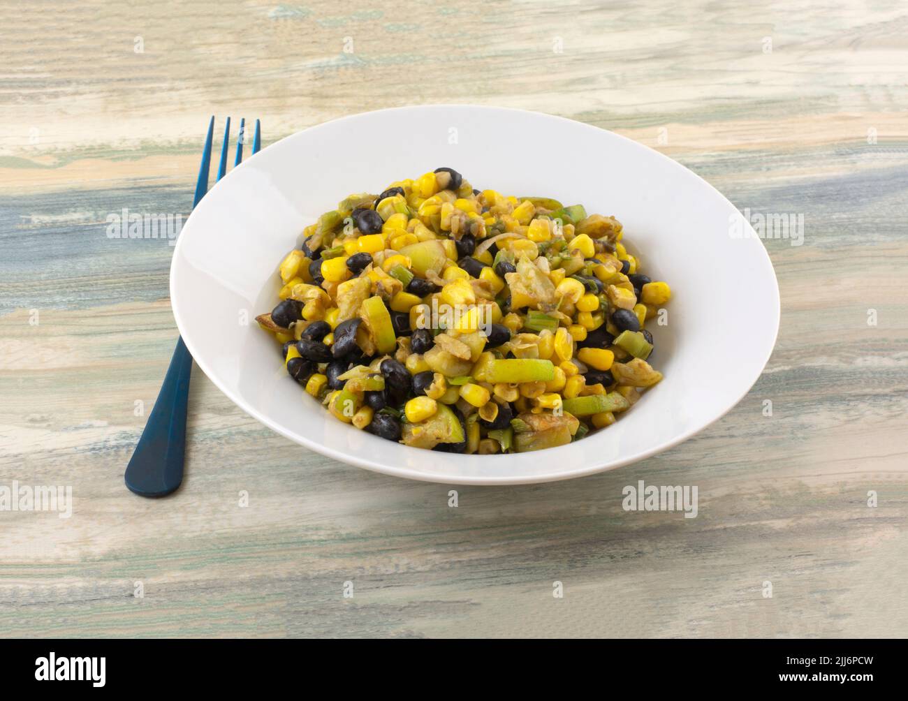 Cooked black beans, corn, and zucchini vegetable side dish or ingredient or filing in white bowl with blue fork Stock Photo