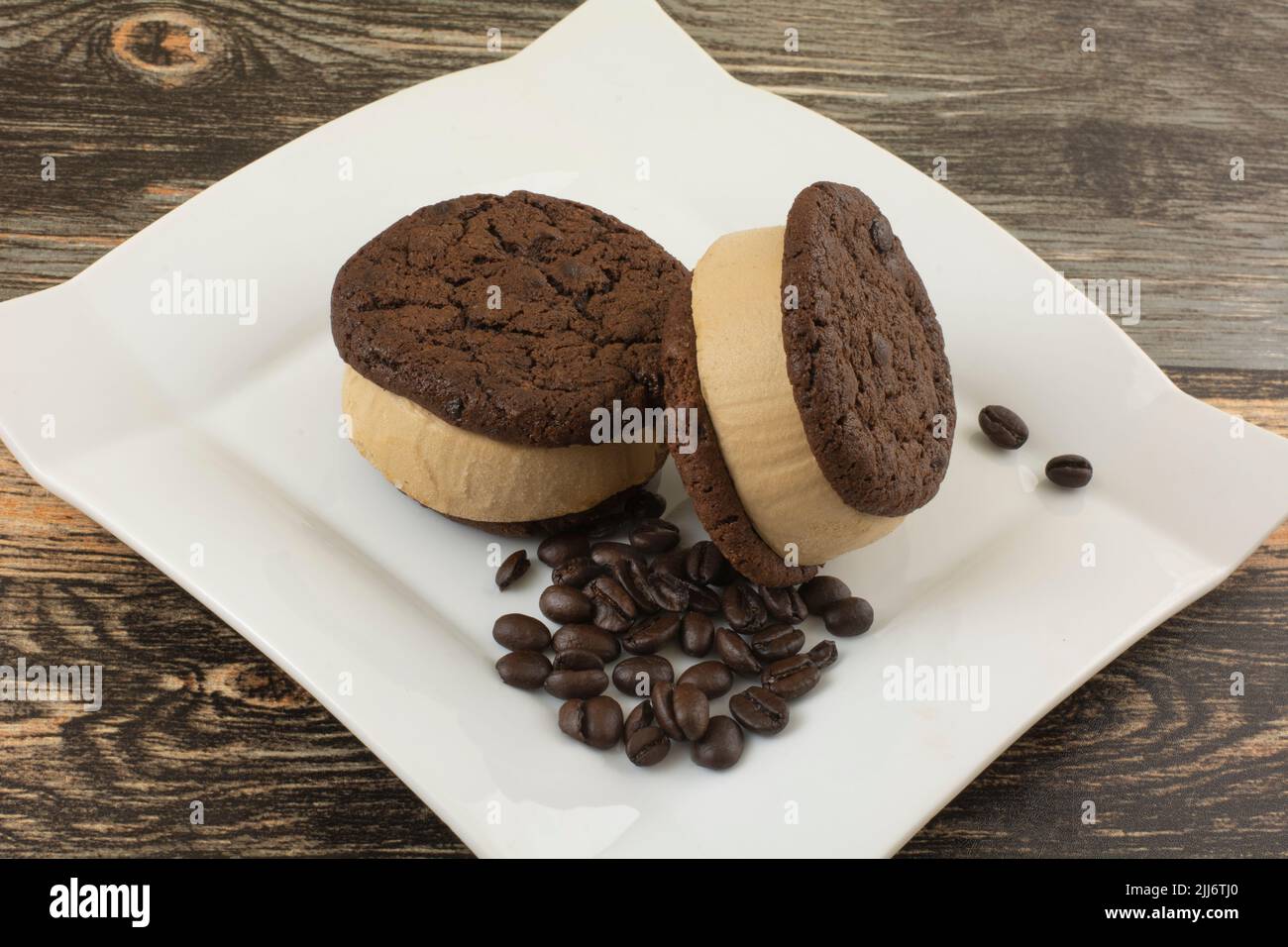 Coffee ice cream sandwich with chocolate cookies on white dessert plate with coffee beans Stock Photo
