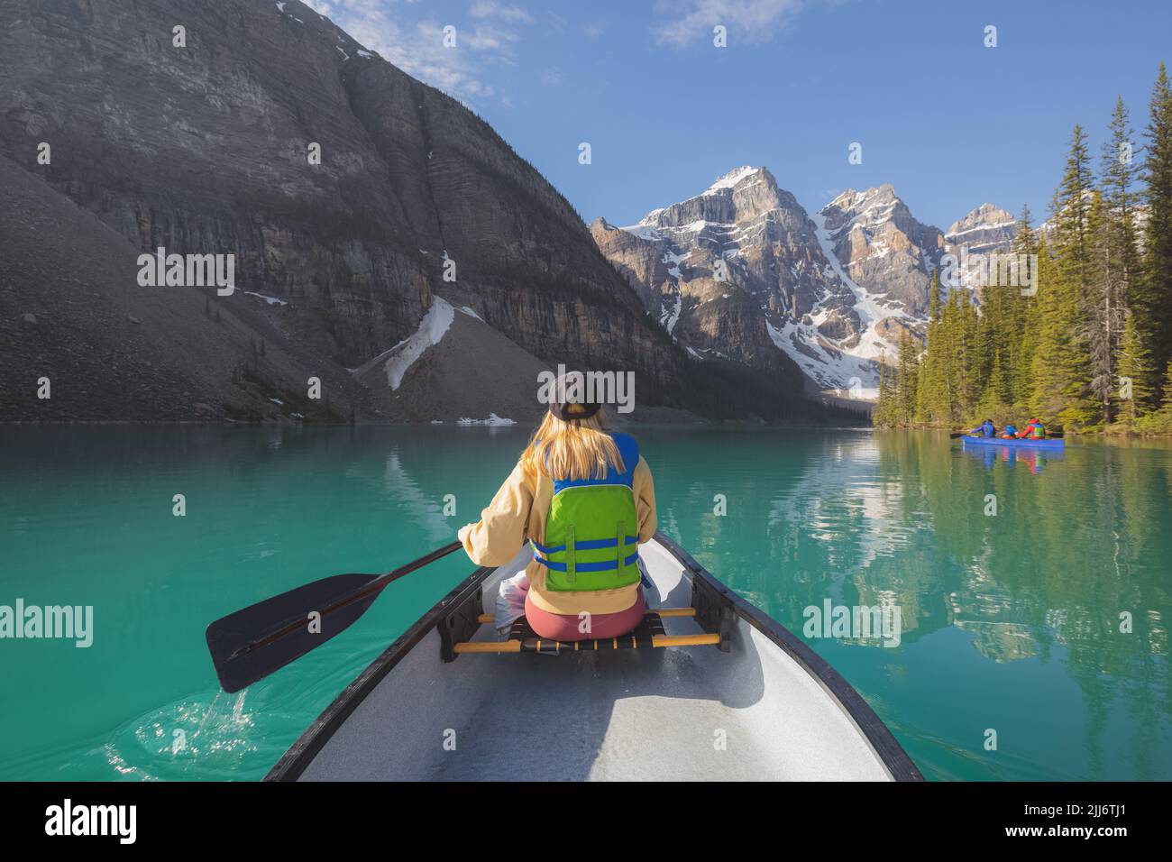 A young blonde woman paddles a canoe on the scenic, picturesque glacial Moraine Lake, a popular outdoor tourist destination in Banff National Park, Al Stock Photo