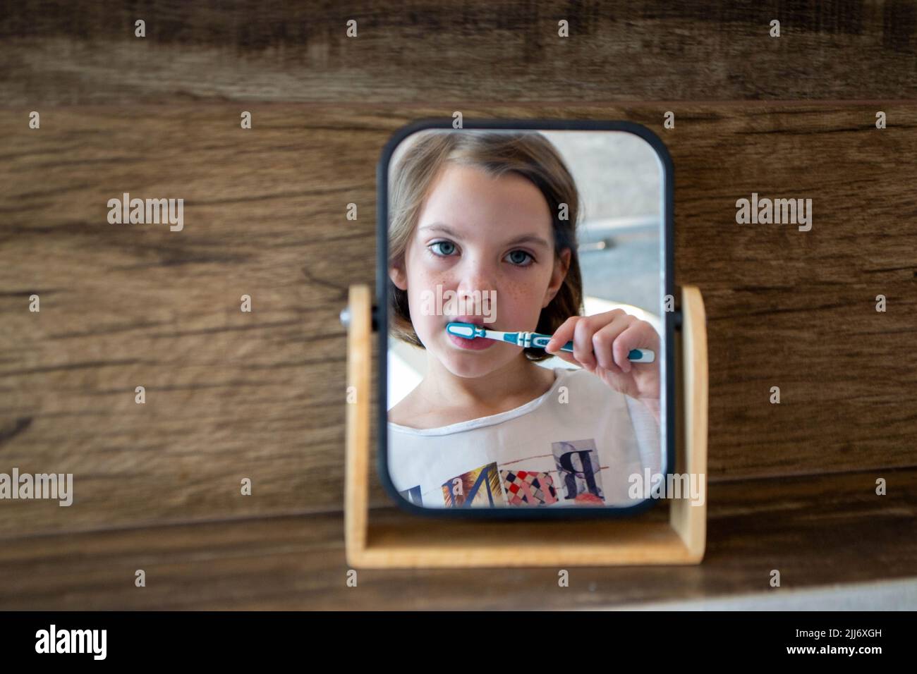 Oral hygiene, healthy teeth and care. Girl brushing teeth with toothbrush and looking in mirror in bathroom interior in the morning, closeup, empty space. High quality photo Stock Photo