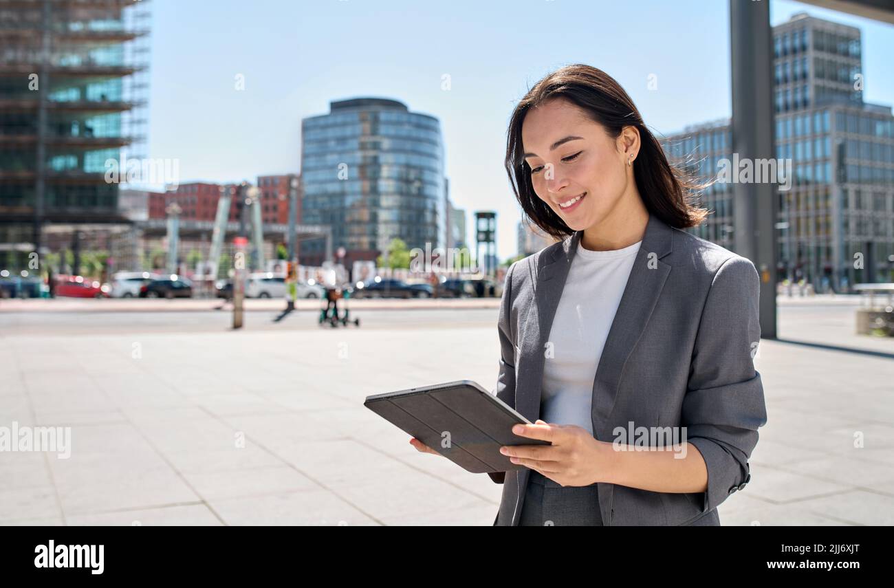 Young happy Asian business woman standing on city street using digital tablet. Stock Photo