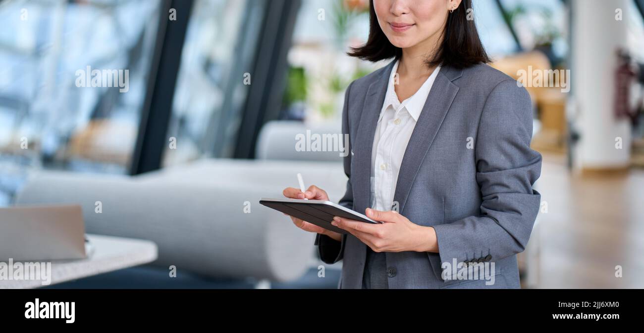 Smiling young Asian business woman leader holding digital tablet in office. Stock Photo