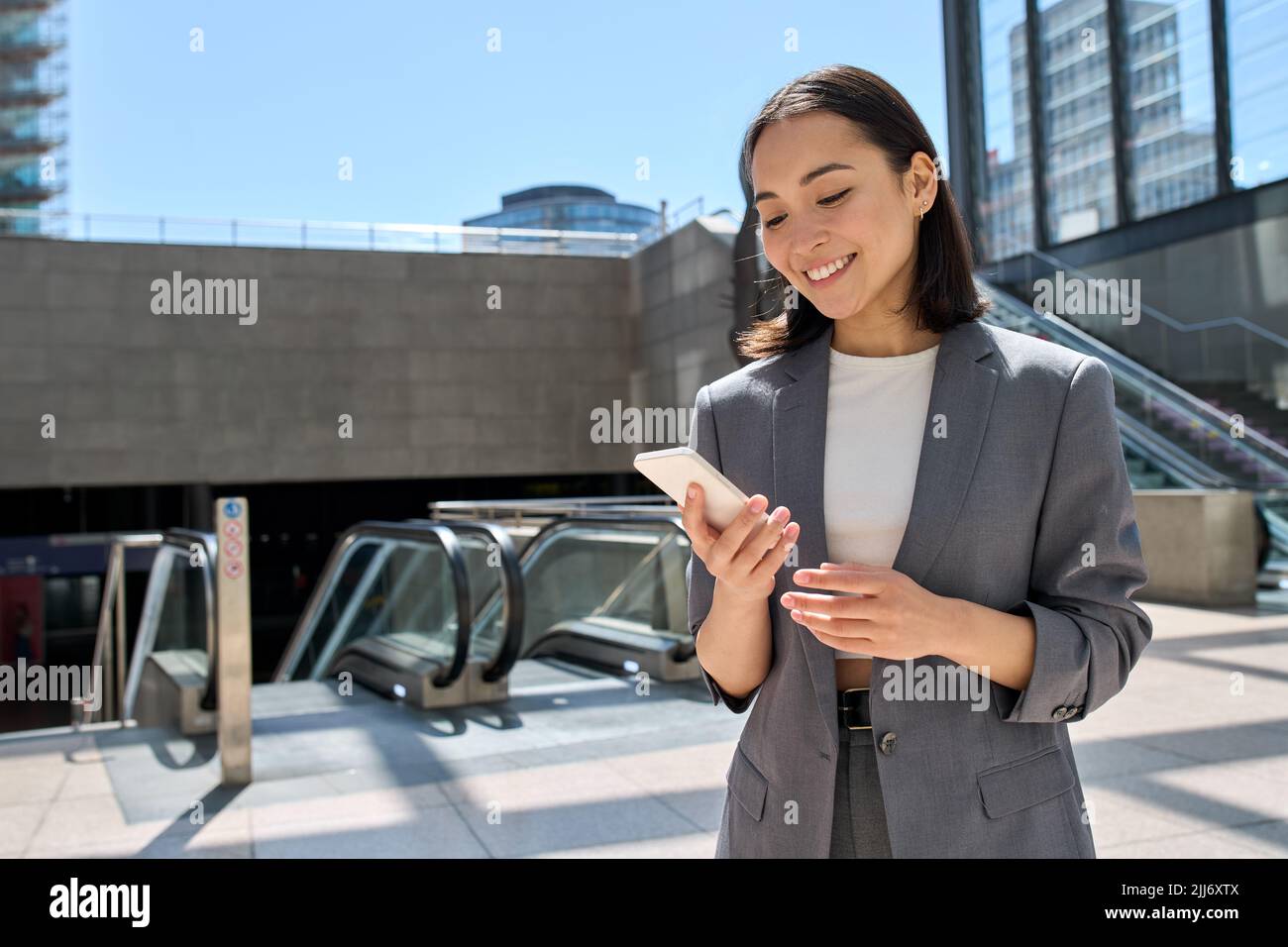 Young happy Asian business woman standing in city subway using smartphone. Stock Photo