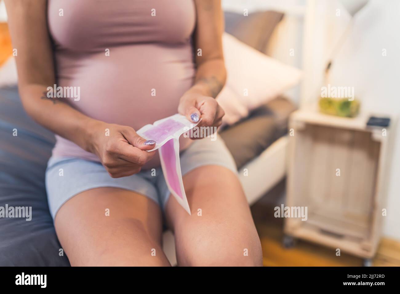 Middle-aged unrecognizable tattooed pregnant woman warming up a wax strips to get rid of her leg hair. Modern beauty standards. High quality photo Stock Photo