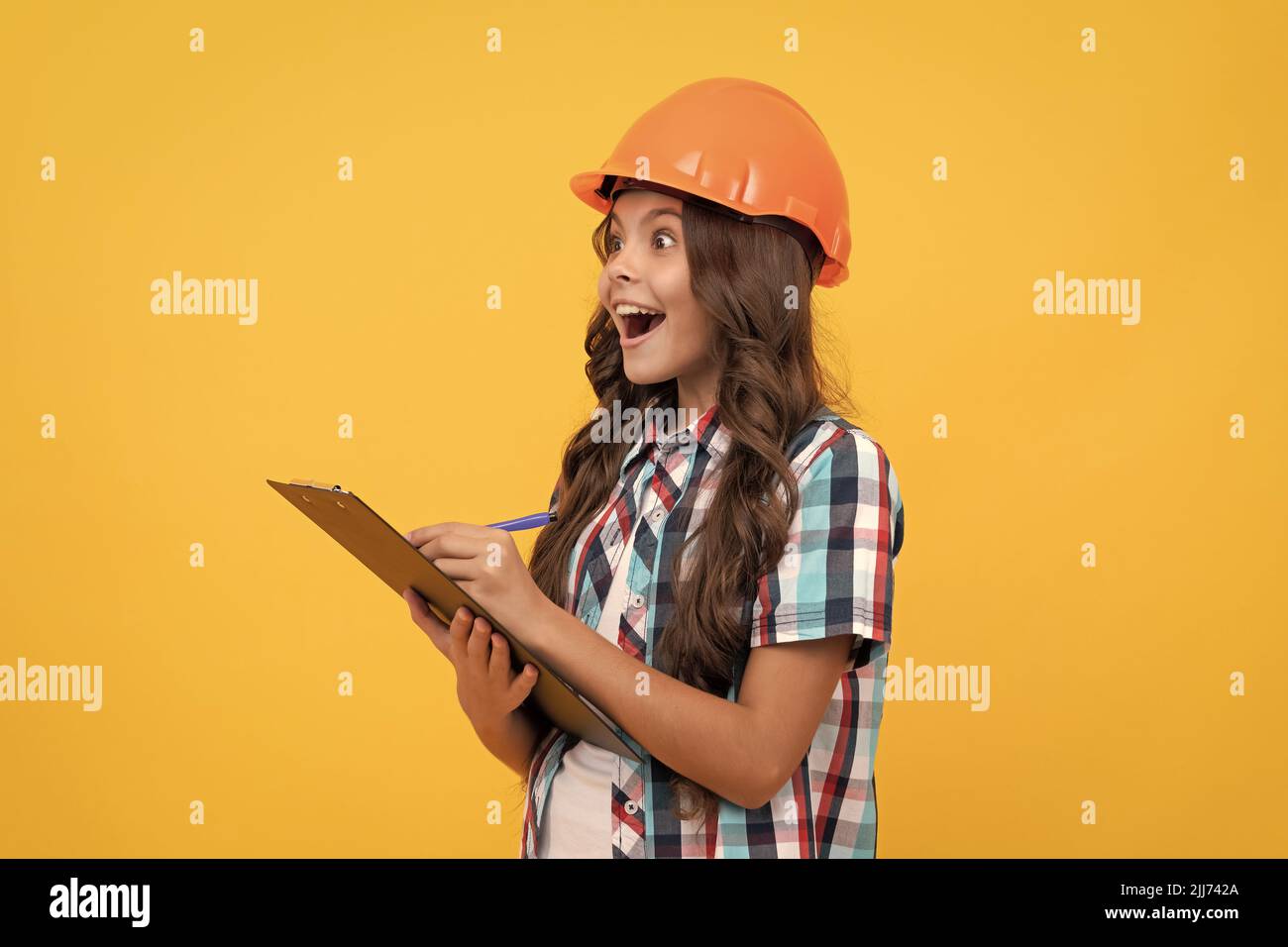 surprised teen girl in construction helmet making notes in clipboard, check results Stock Photo