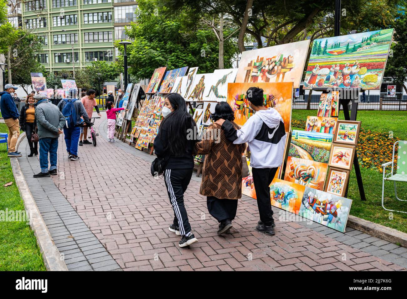 A family walks together past local artists works in Parque Kennedy on a Sunday afternoon. Stock Photo