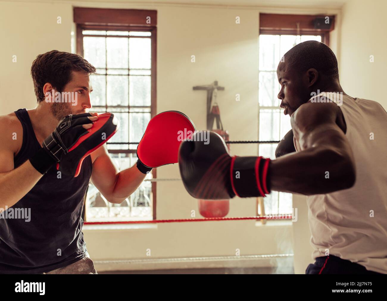 Young boxing coach training a young boxer with focus pads in a gym. Physical trainer teaching a young boxer punching techniques in a boxing ring. Stock Photo