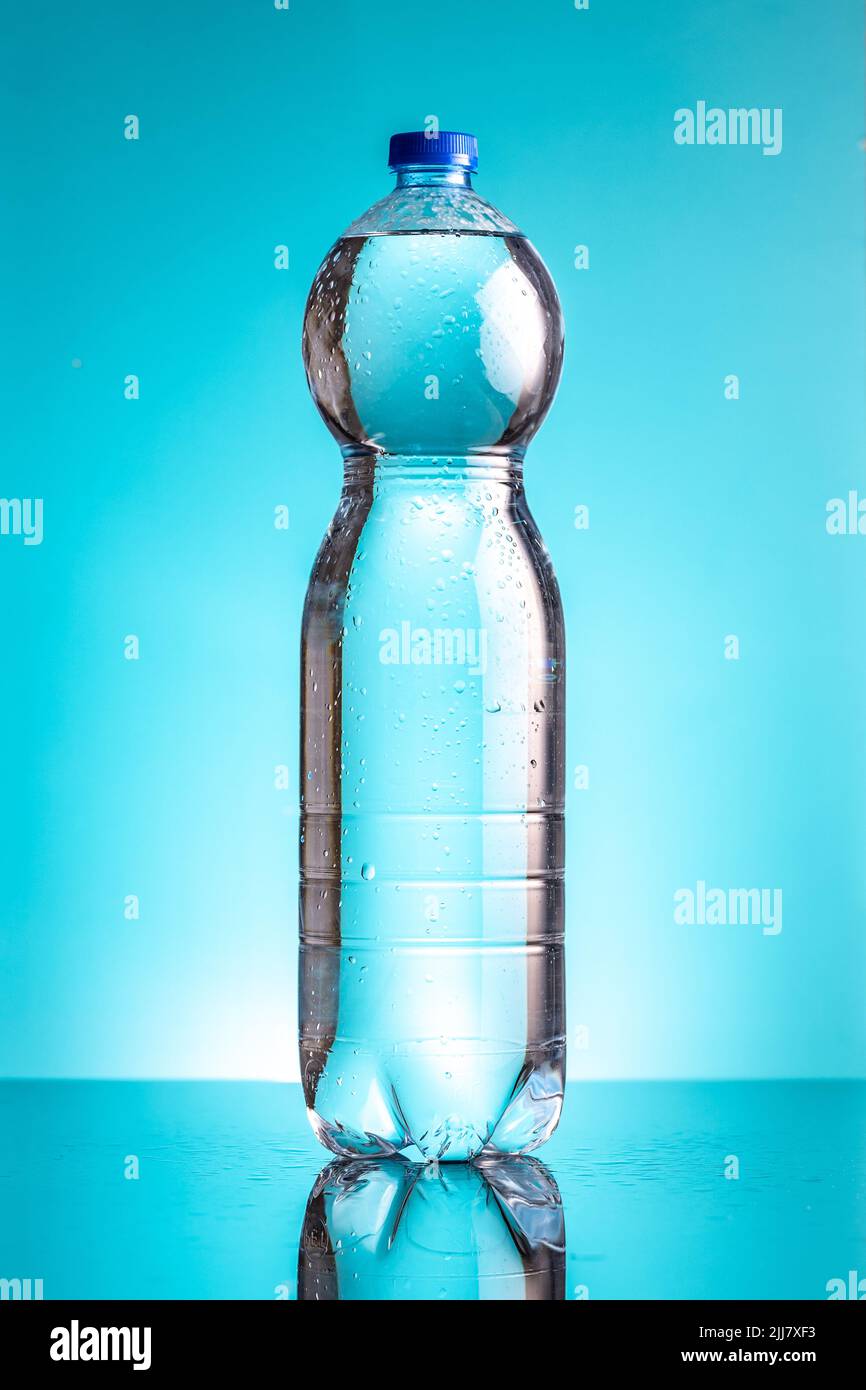 Plastic cold bottle of water with water drops on a blue background. Stock Photo