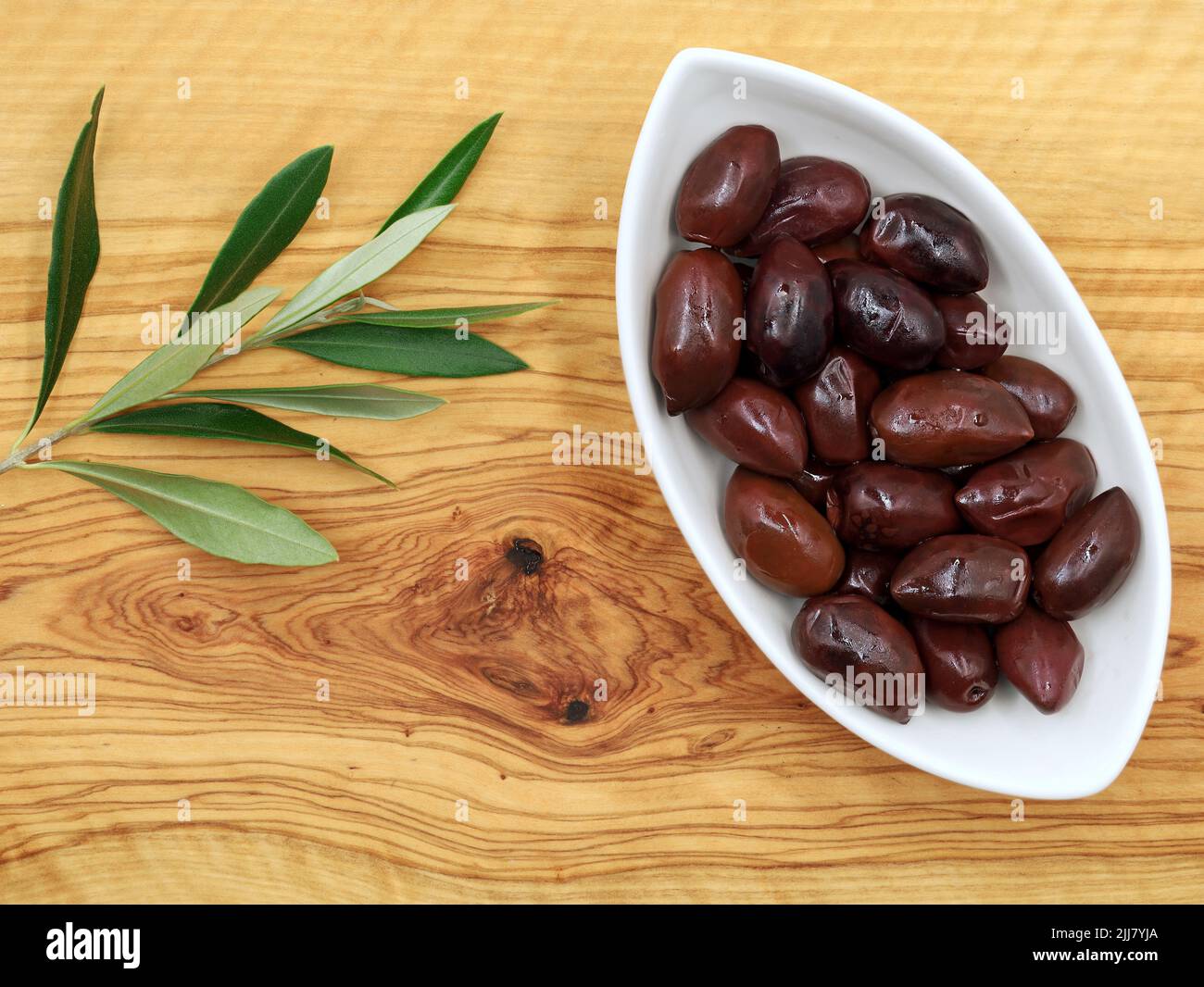 Kalmata olives in white bowl on olive wooden board with branch, top view Stock Photo
