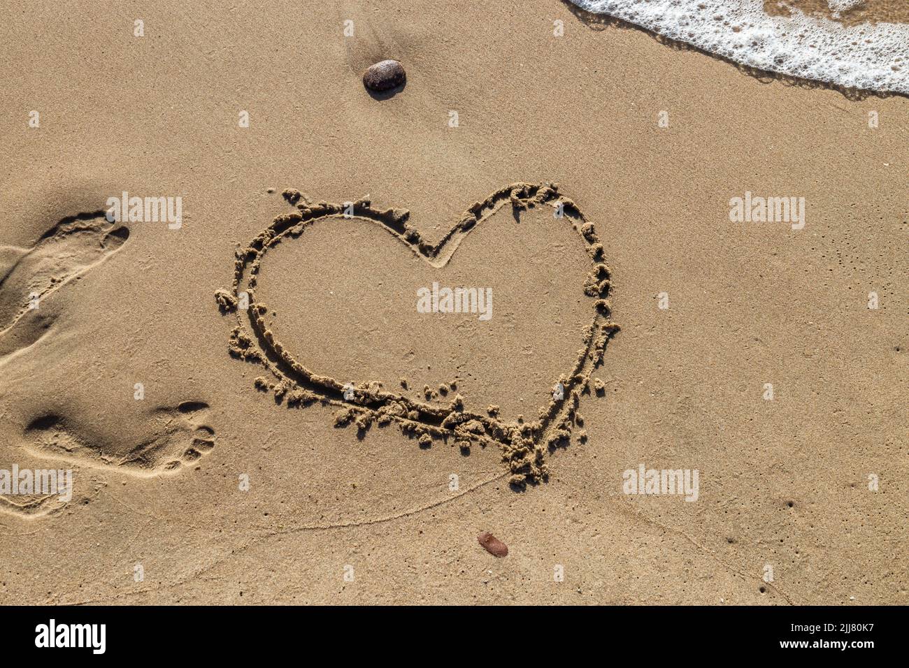 Heart handwritten on the sand on the beach and foam from the waves ...