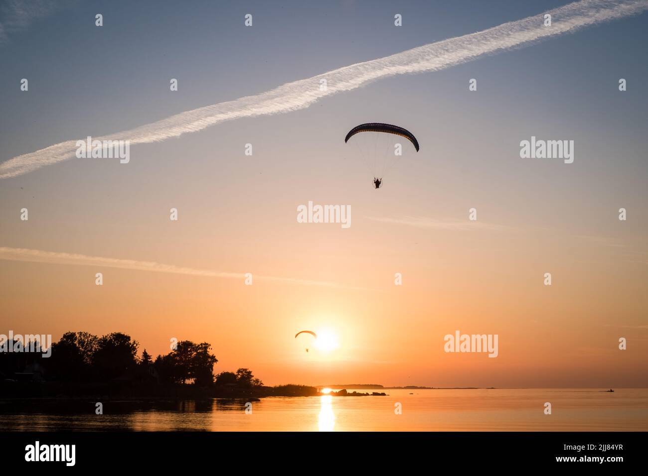Two paraglider pilots fly in the sky during sunset on beautiful beach. Paraplanes silhouettes. Adventure vacation and travel concept. Stock Photo