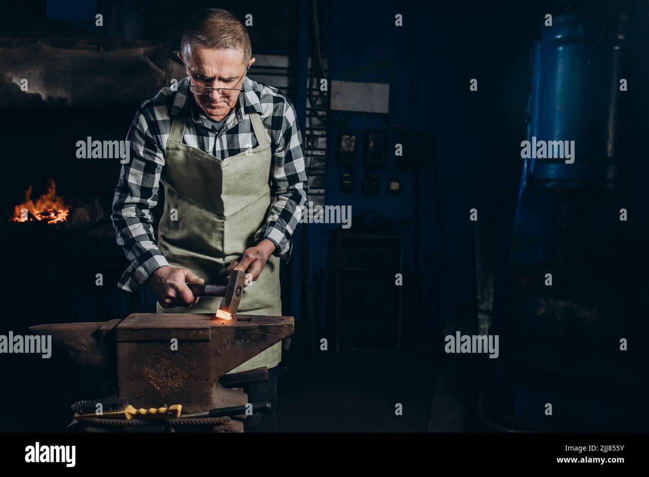 The blacksmith manually forging the red-hot metal on the anvil in smithy. Hard work. Energy and power. Concept of labor, retro professions Stock Photo