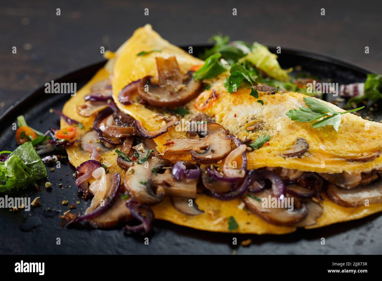 Closeup of delicious omelet with mushrooms and herbs served on table for lunch Stock Photo