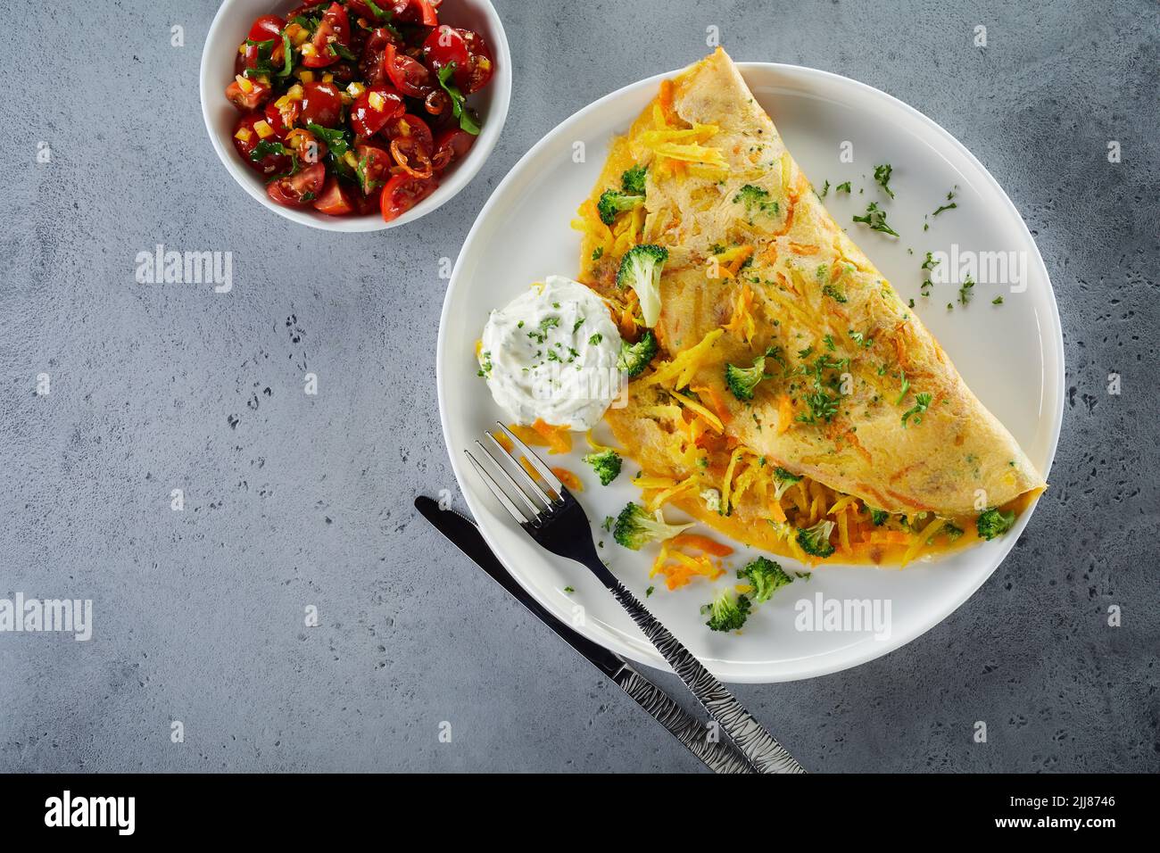 Top view of nutritious omelet with vegetables and delicious salad in bowl placed on gray table for lunch Stock Photo