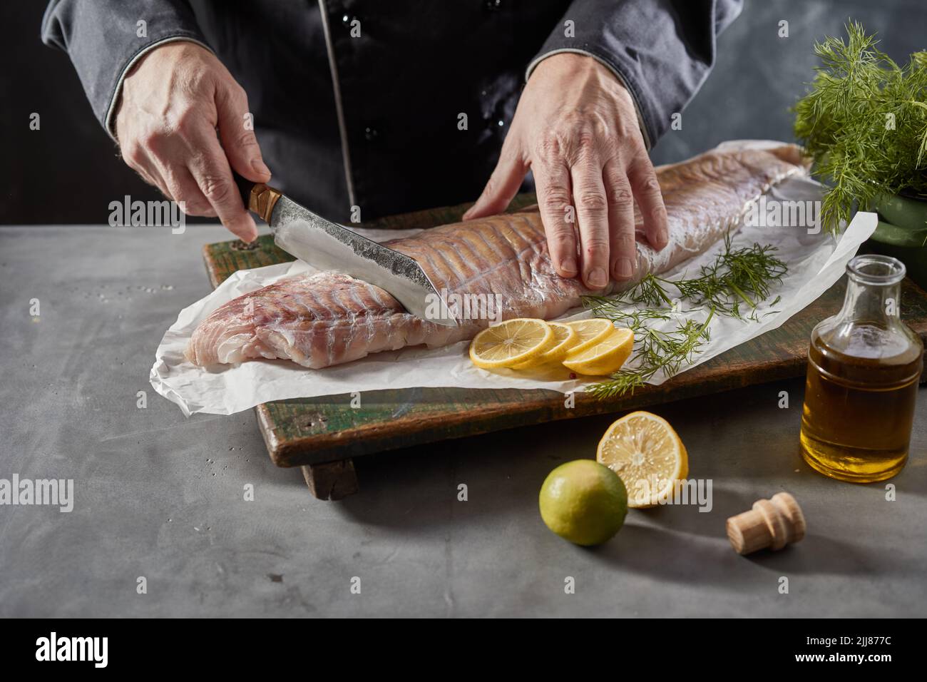 From above of faceless crop male chef cutting fresh fish fillet on chopping board while cooking in kitchen Stock Photo