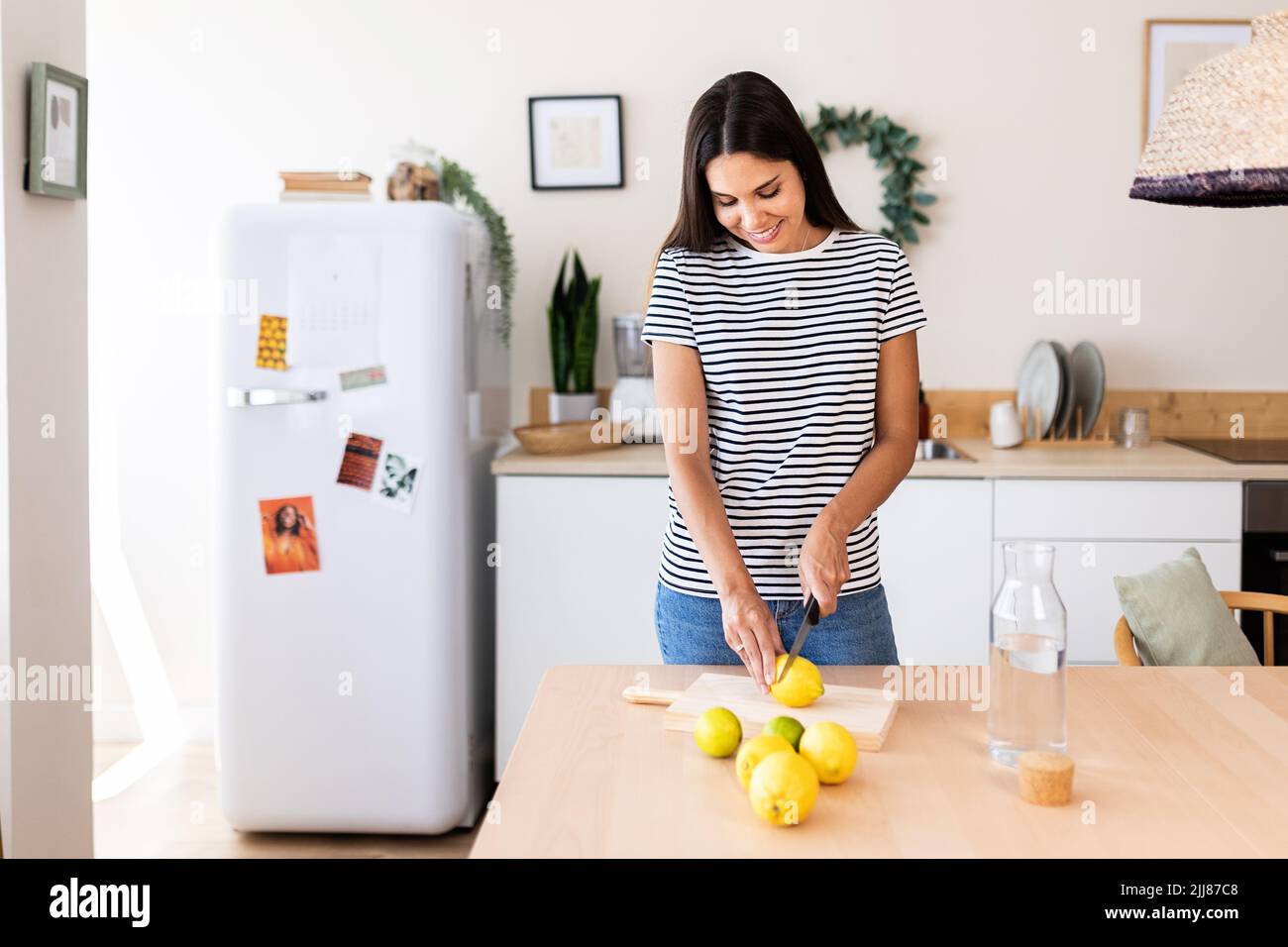 Serene young adult woman preparing homemade lemon juice in the kitchen at home Stock Photo