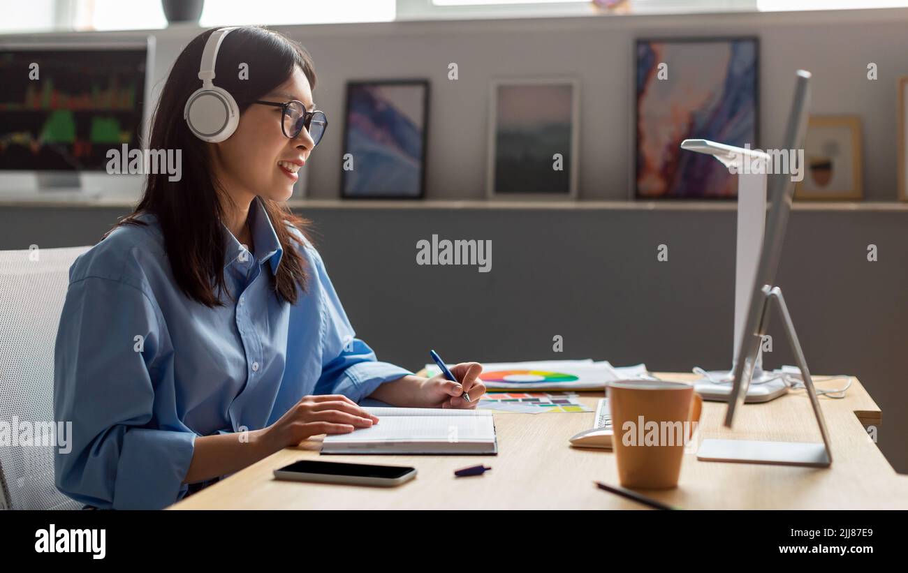 Asian Lady Working Online On Computer Taking Notes At Workplace Stock Photo