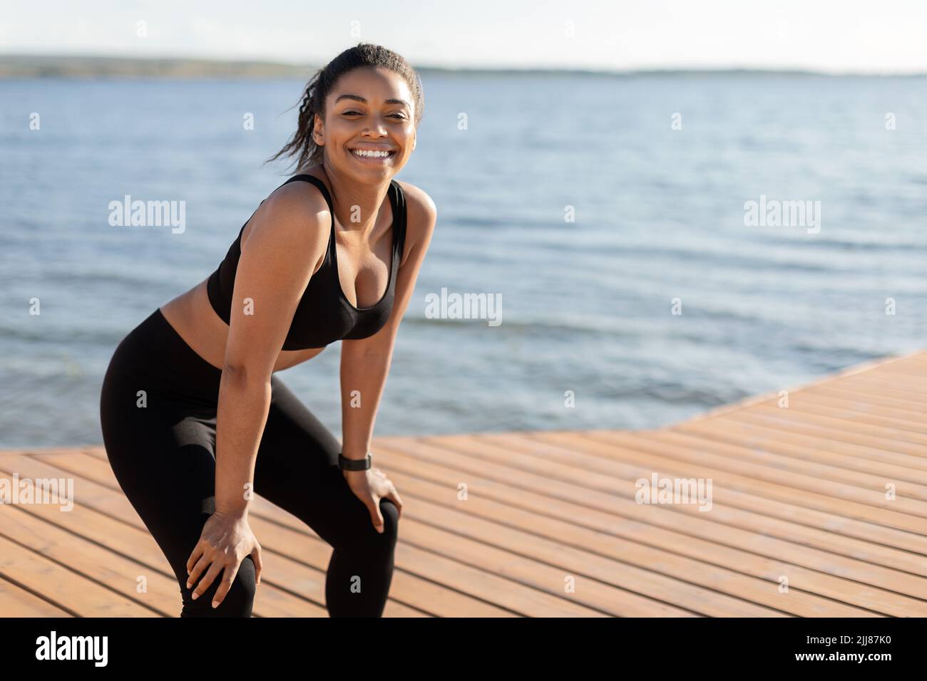 Cheerful african american lady training by seaside, having break Stock Photo
