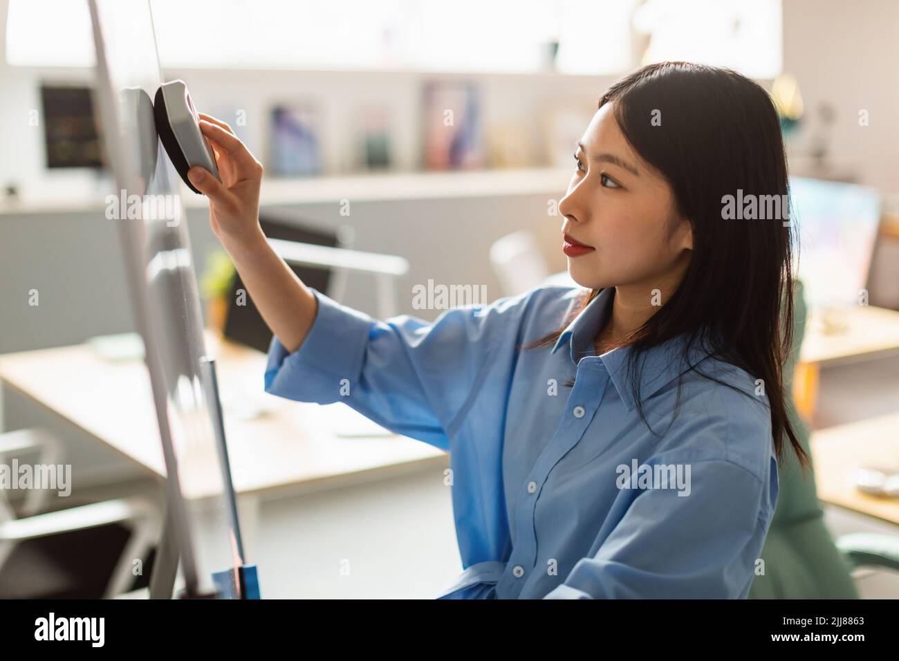 Japanese Businesswoman Wiping Flipchart Board Preparing Presentation At Workplace Stock Photo