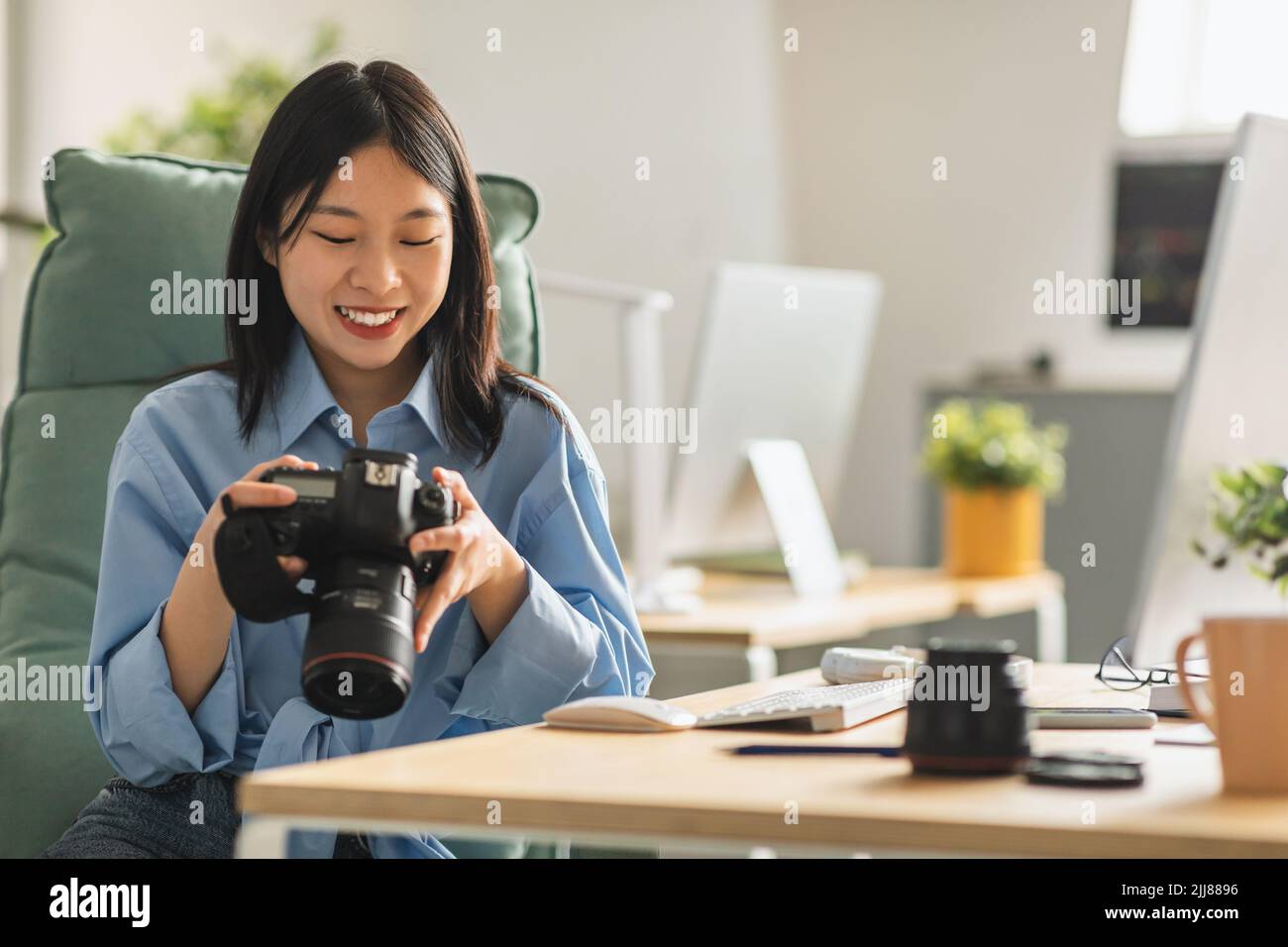 Cheerful Japanese Lady Photographer Holding Photocamera At Workplace Indoor Stock Photo