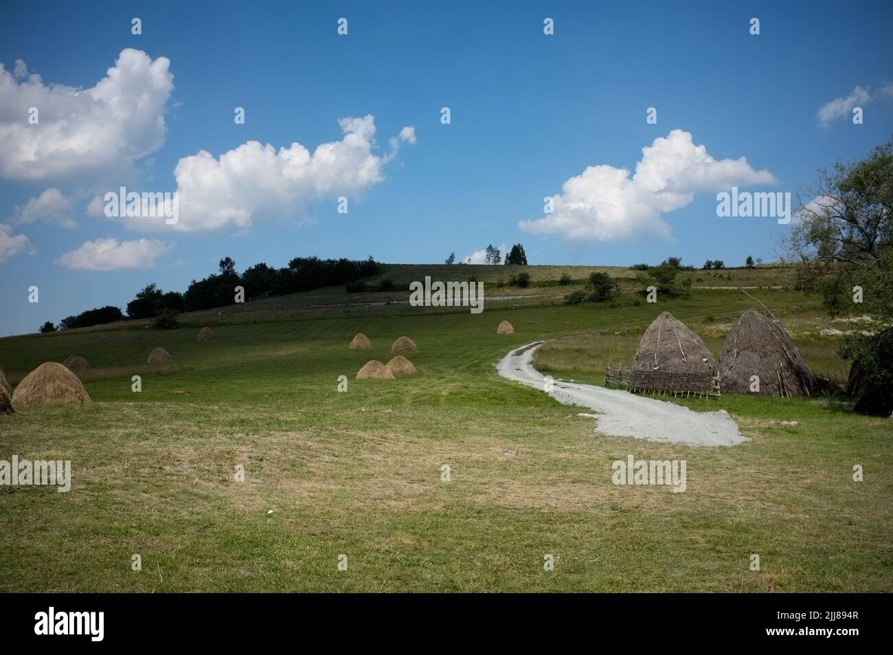 clouds sky on haystacks in a meadow of Serbia with winding path Stock Photo