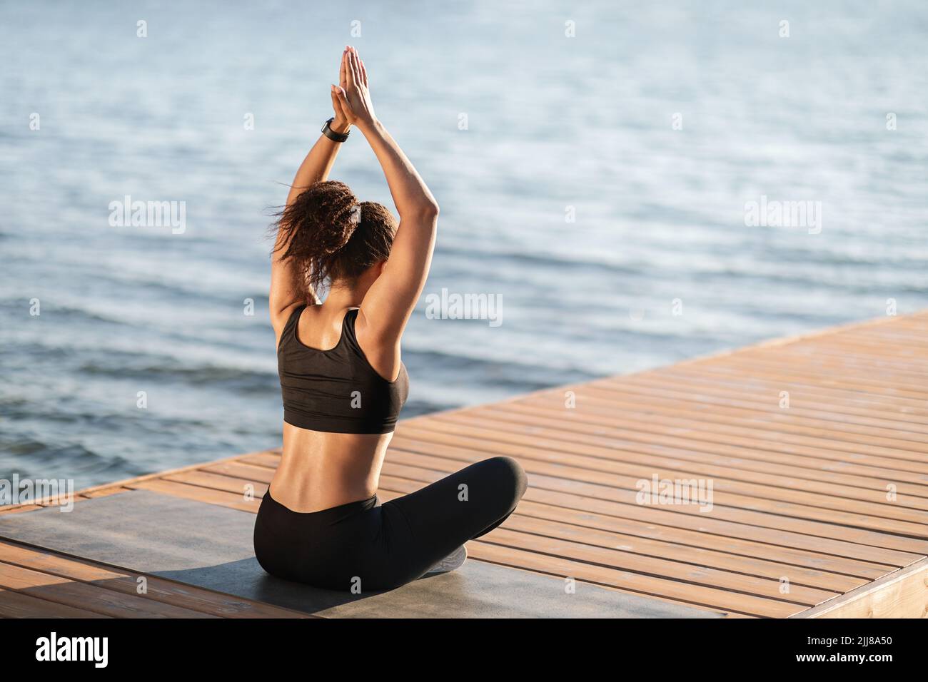 Unrecognizable african american woman meditating by water, rear view ...