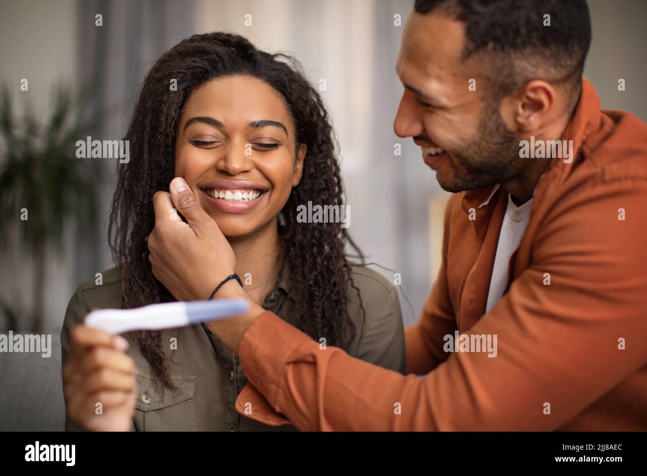 joyful-black-couple-holding-pregnancy-test-sitting-on-sofa-indoors