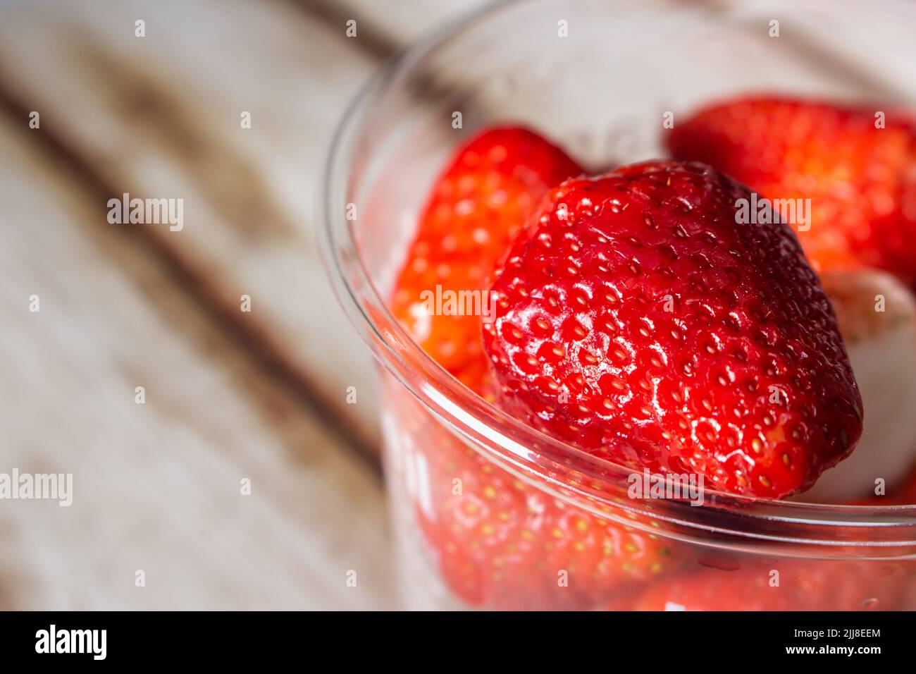 Closeup of strawberries in a plastic cup on a wooden shabby chic table. Stock Photo