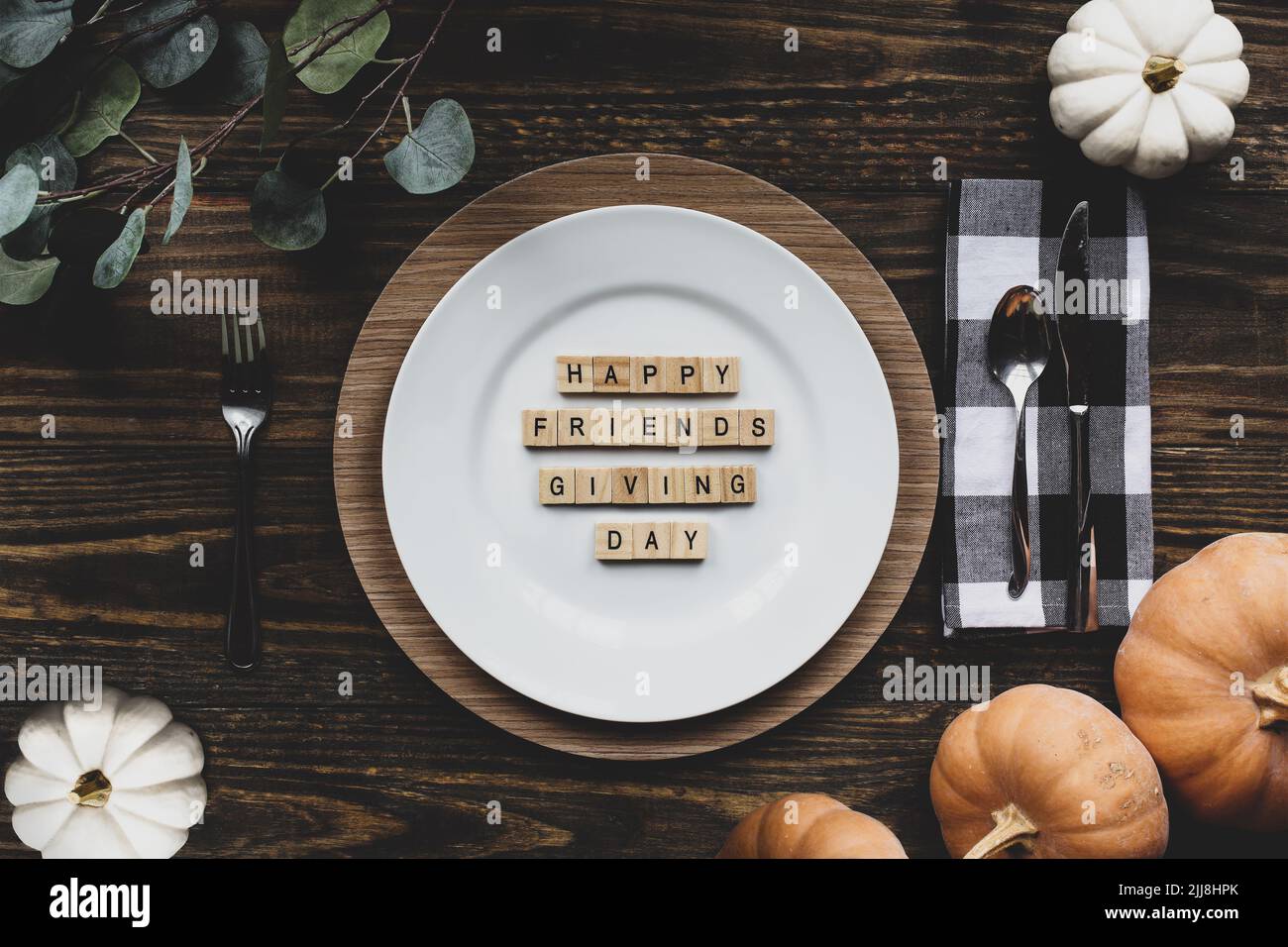 Thanksgiving place setting with plate, napkin, on a  decorated table shot from flat lay or top view position. Happy Friendsgiving Day spelled out with Stock Photo