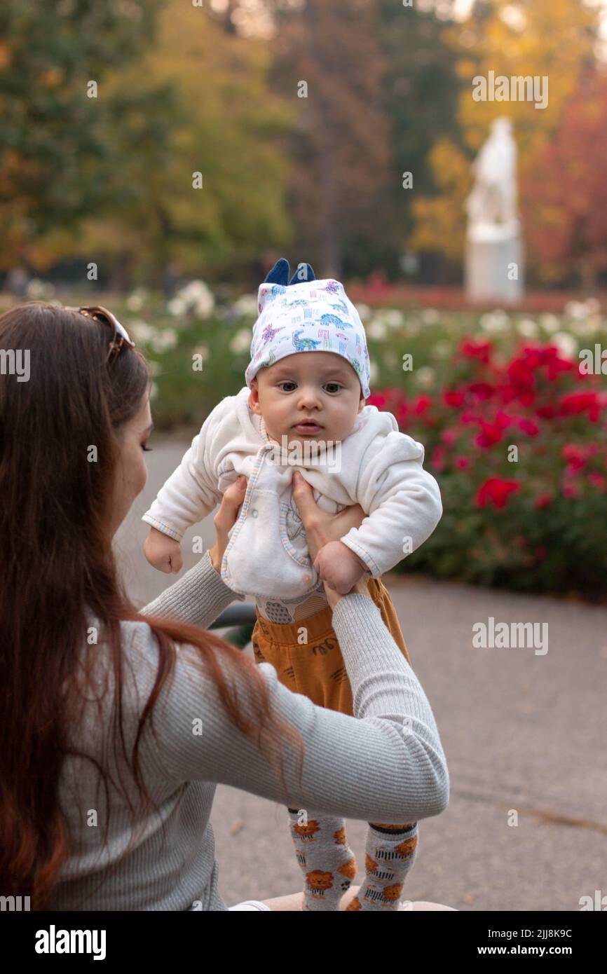 Mother raising up 6 months old baby in her hands outside in the park Stock Photo